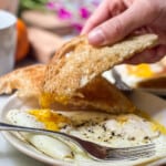 Over easy eggs on a small plate with toast being dipped into the runny yolk