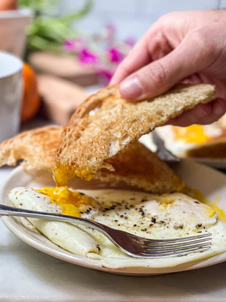 Over easy eggs on a small plate with toast being dipped into the runny yolk