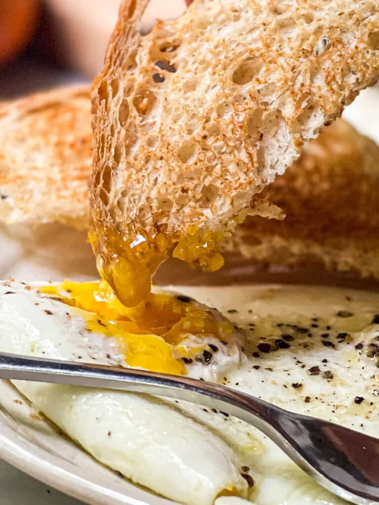 Over easy eggs on a small plate with toast being dipped into the runny yolk