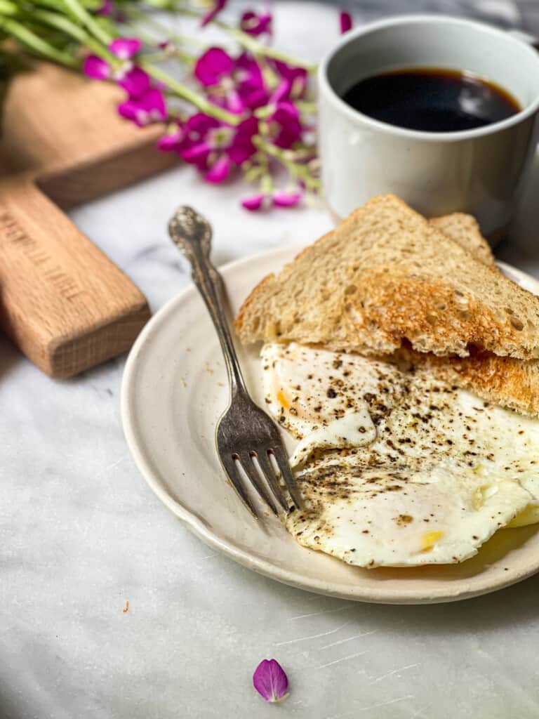 Over easy eggs on a small plate with toast being dipped into the runny yolk