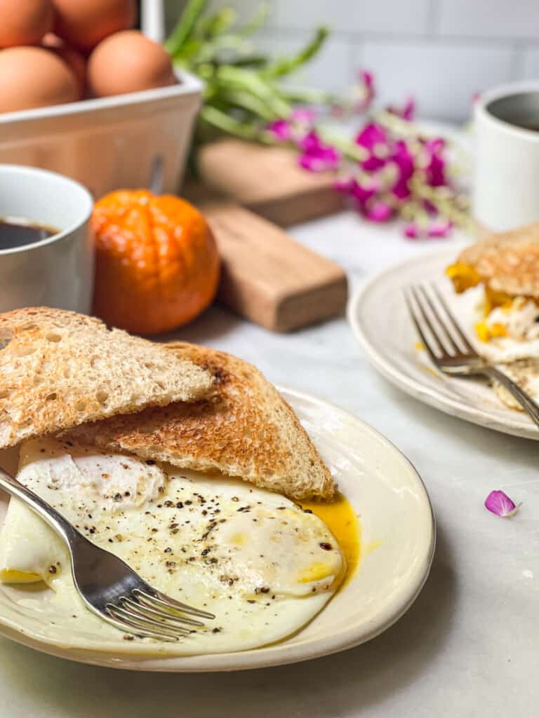 Over easy eggs on a small plate with toast being dipped into the runny yolk