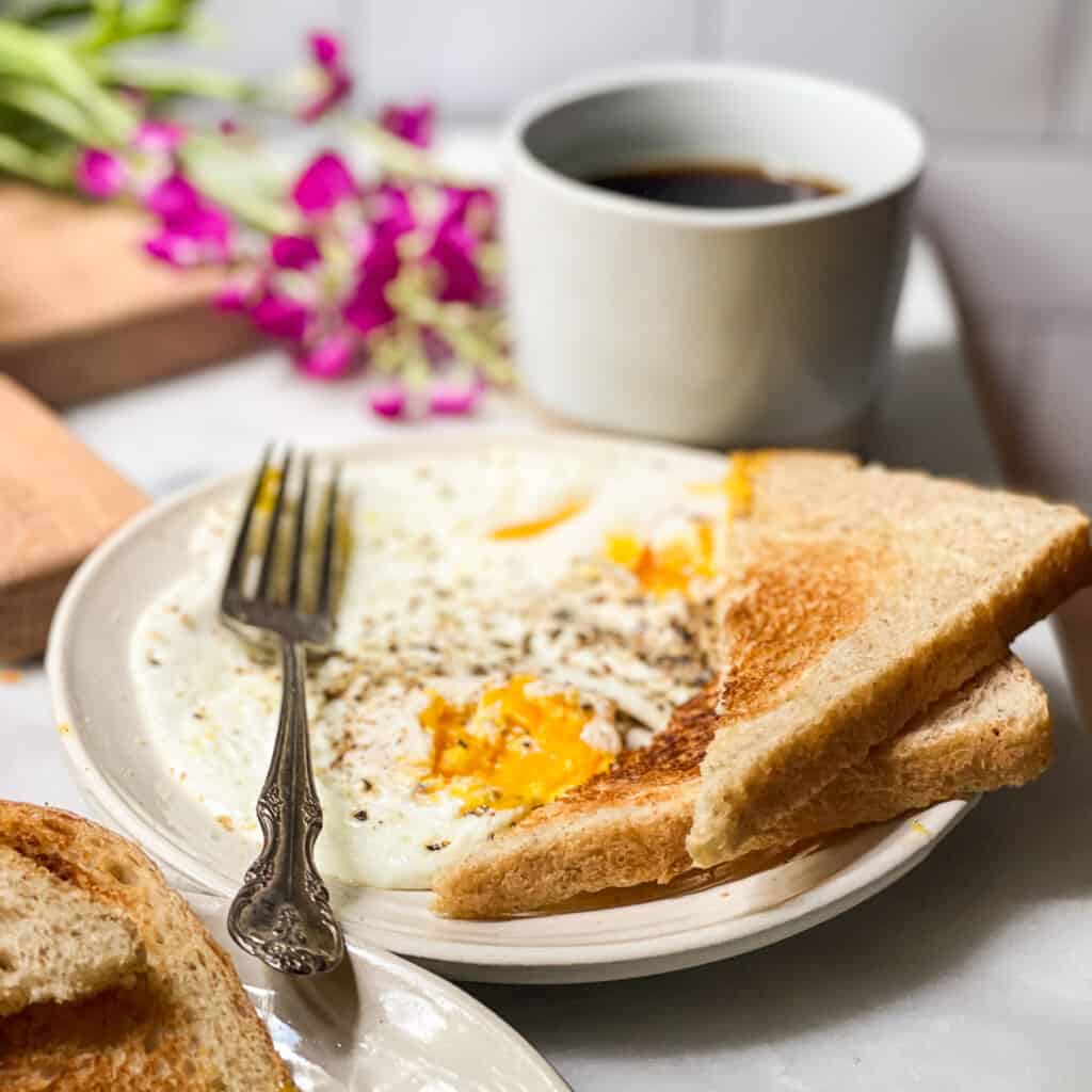 Over easy eggs on a small plate with toast being dipped into the runny yolk