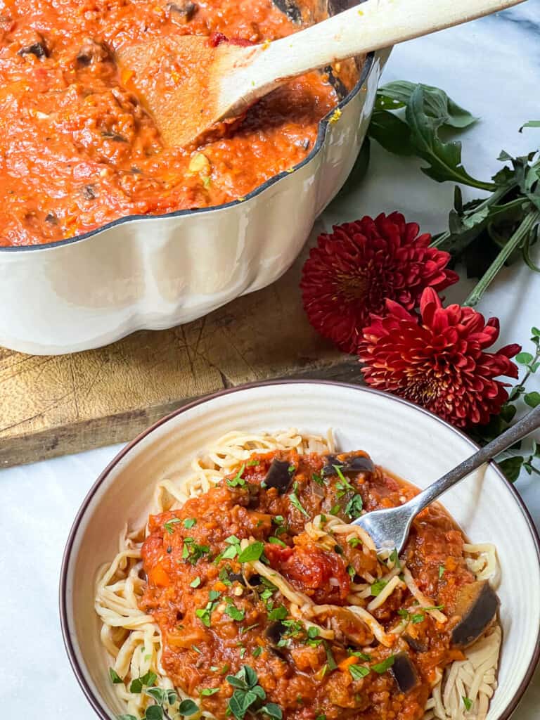 Bowl of vegetarian bolognese next to a large dutch oven filled with bolognese sauce