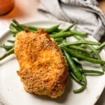 Glutenfree breaded air fryer pork chops and green beans on two plates (one plate is white and the other one is peach in color)