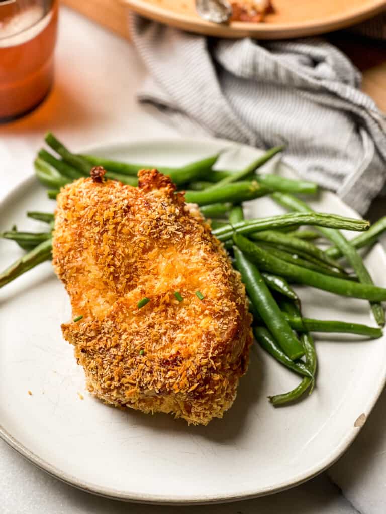 Glutenfree breaded air fryer pork chops and green beans on two plates (one plate is white and the other one is peach in color)