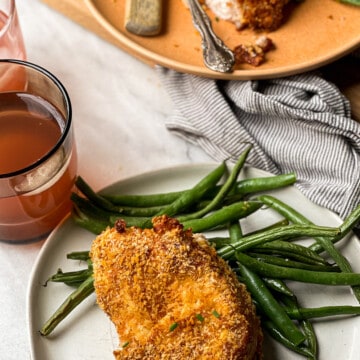 Glutenfree breaded air fryer pork chops and green beans on two plates (one plate is white and the other one is peach in color)