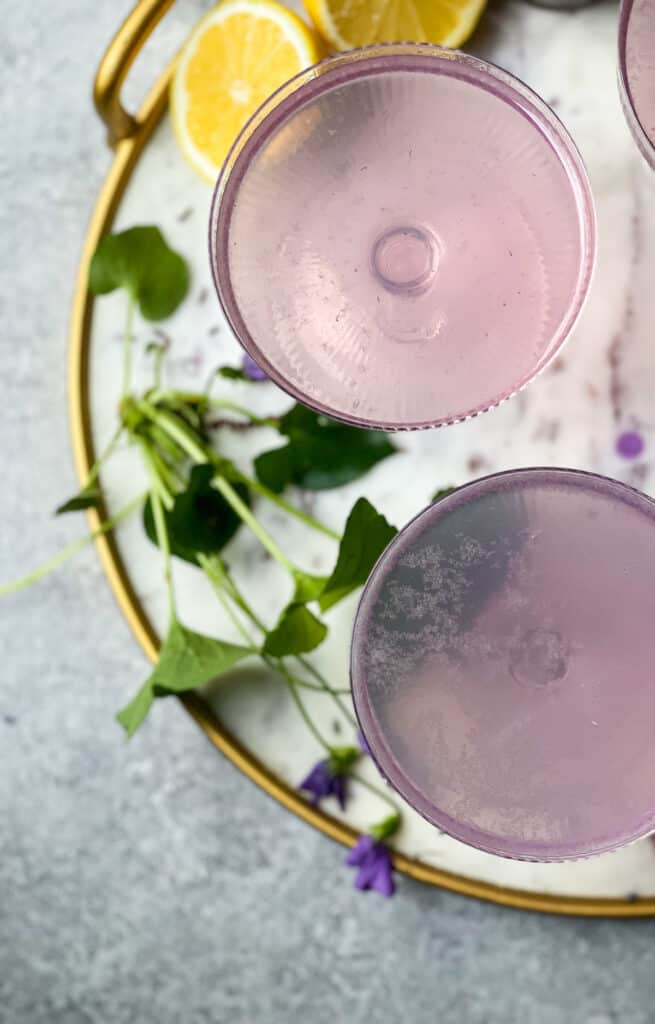 Lavender French 75 Cocktail in 3 glass art deco style glassware on a round white marble tray with a gold rim - The Kitcheneer