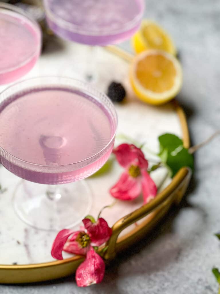 Lavender French 75 Cocktail in 3 glass art deco style glassware on a round white marble tray with a gold rim - The Kitcheneer 